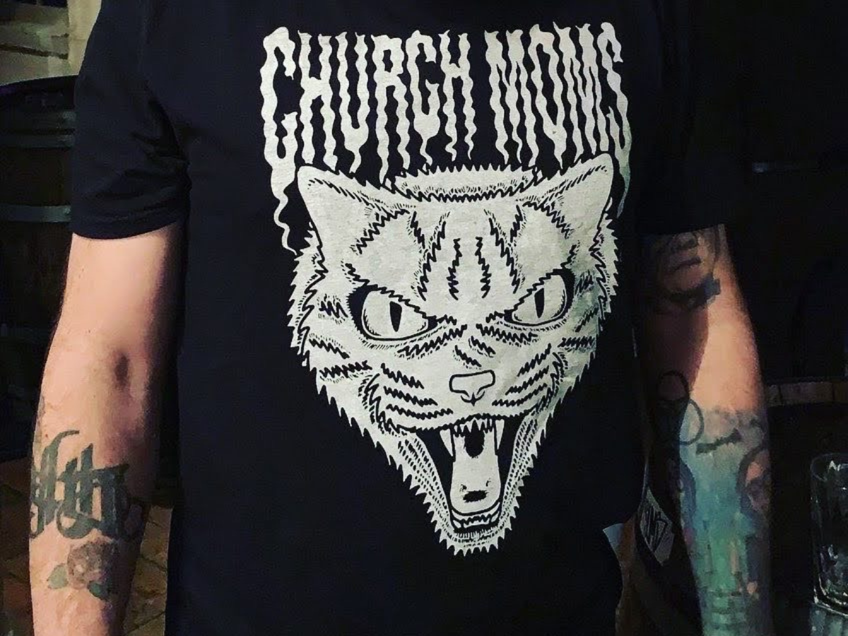 the Church Moms snarling cat logo in white on a black t-shirt